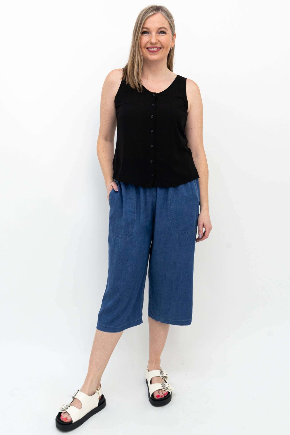 Woman wearing relaxed fit blue denim Tencel capris and black sleeveless top