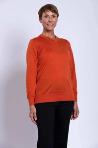 Woman wearing a tangerine V-neck merino wool sweater with black pants, smiling.