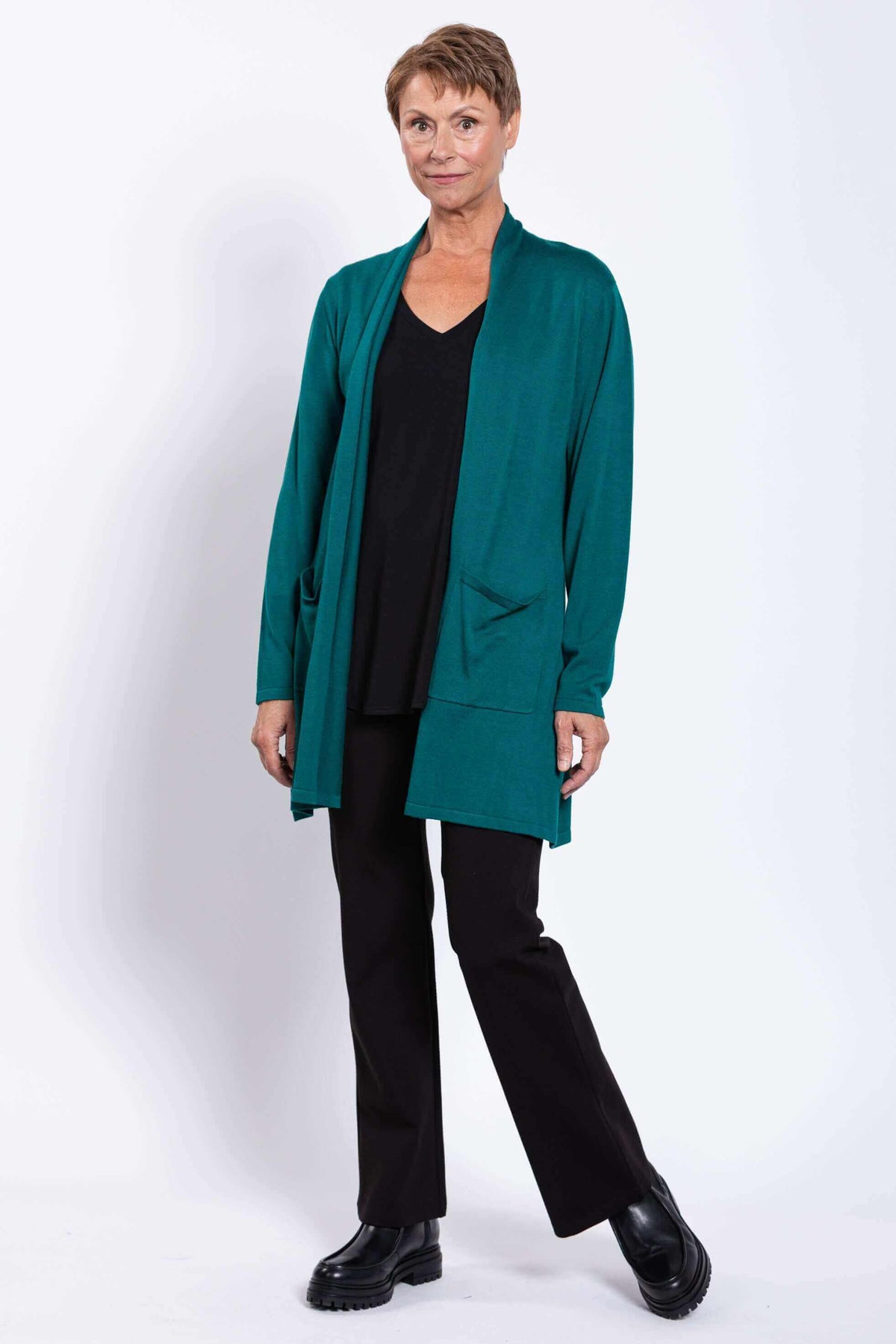 Woman modeling teal open cardigan, black outfit, standing at slight angle