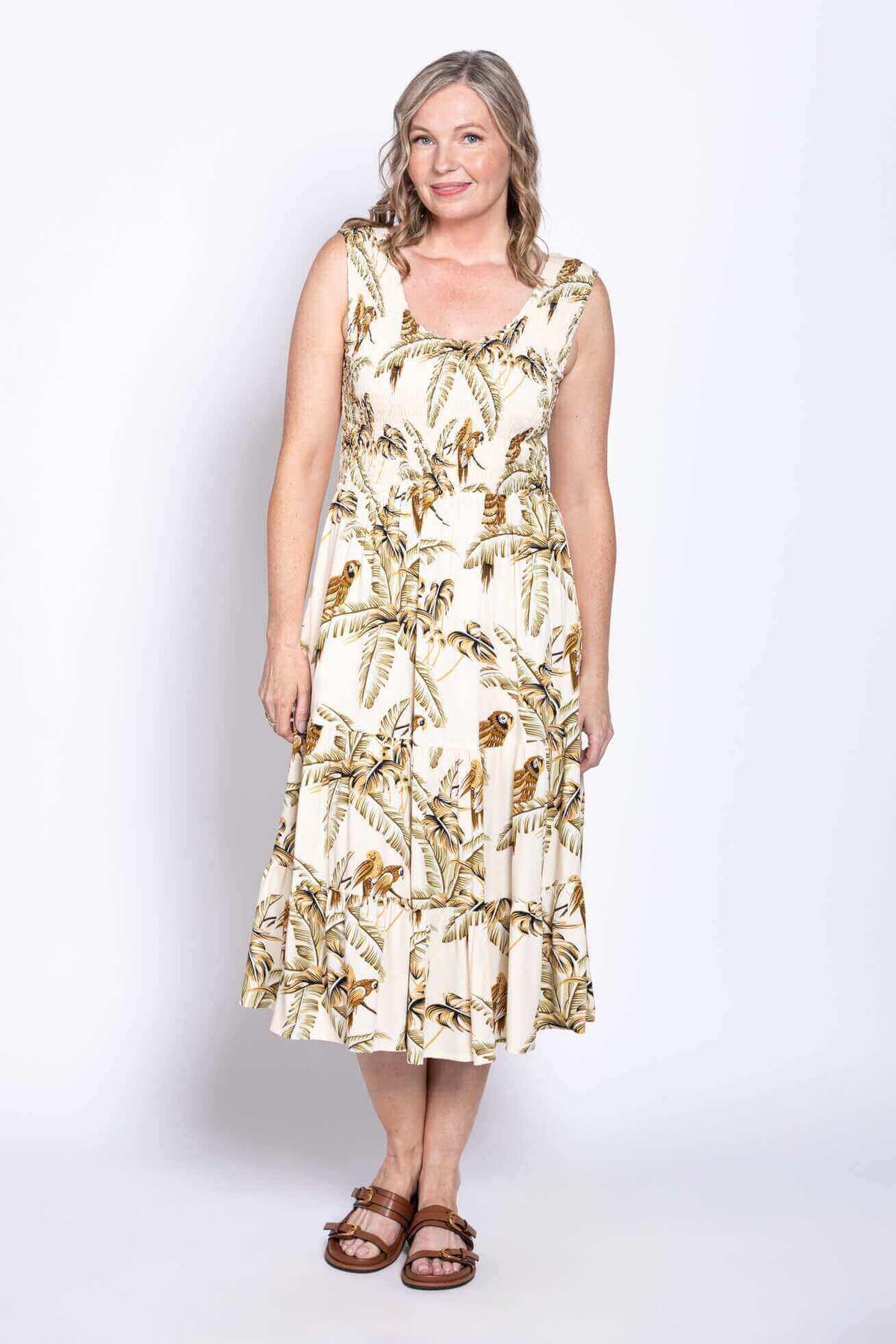 Woman wearing sleeveless tropical print midi dress, smiling with one foot forward