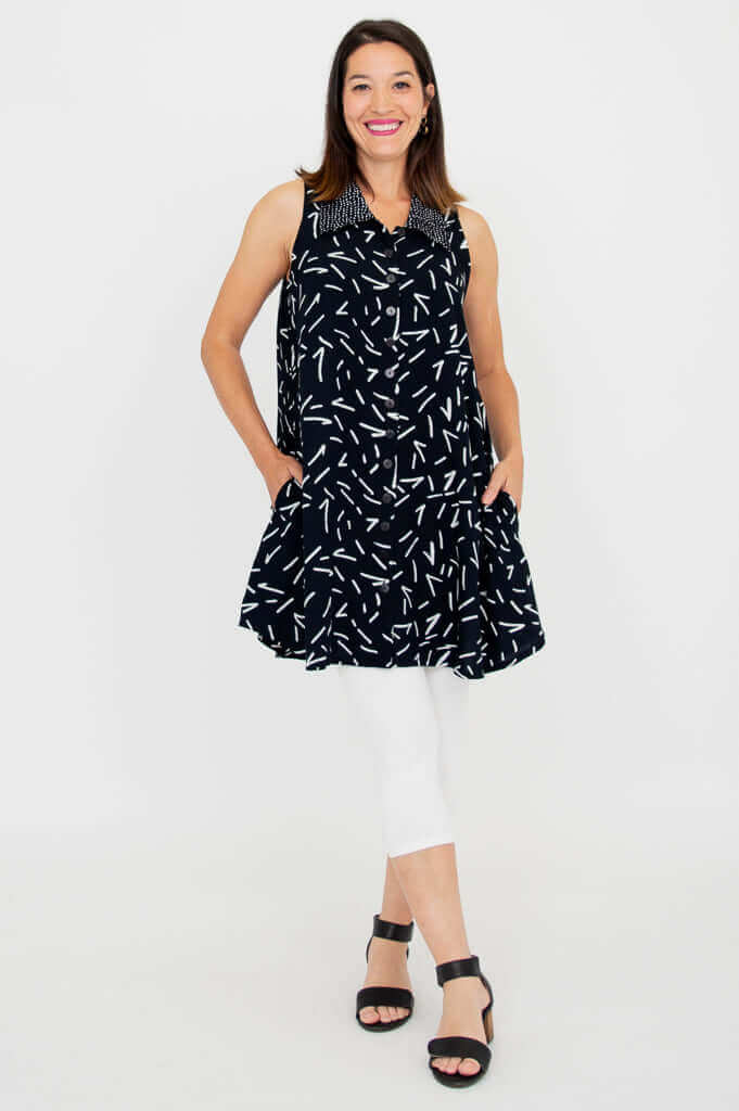 Woman models black sleeveless dress with white dash print and side pockets