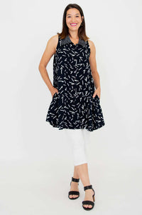 Woman models black sleeveless dress with white dash print and side pockets