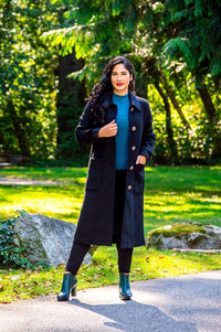 Woman outdoors in a black knee-length coat with large buttons and patch pockets