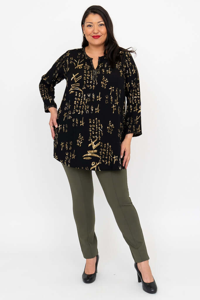 Woman posing hands on hips in black batik blouse and slim olive pants
