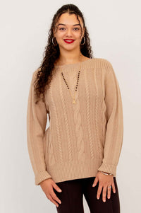 Woman in beige cable knit sweater poses with hands slightly forward