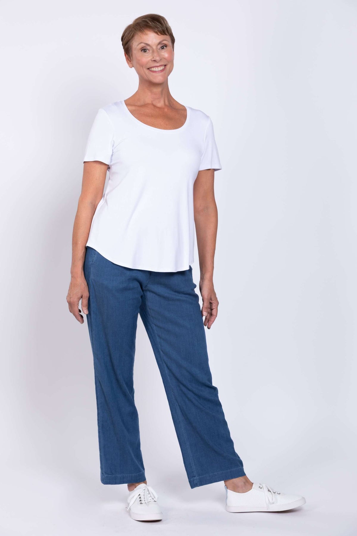 Woman posing in blue pants, white sneakers, and a short sleeve white tee