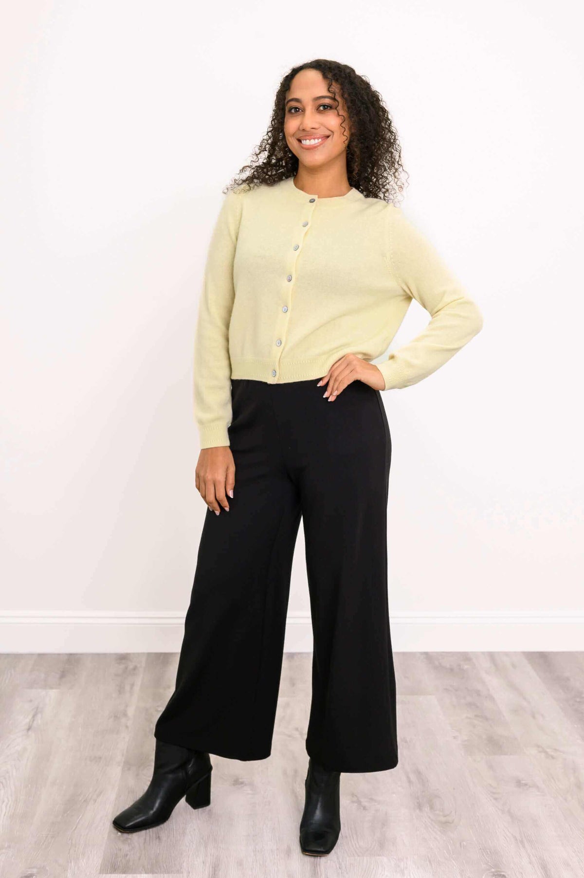 Woman posing in a light yellow cashmere cardigan and black pants, right hand on hip