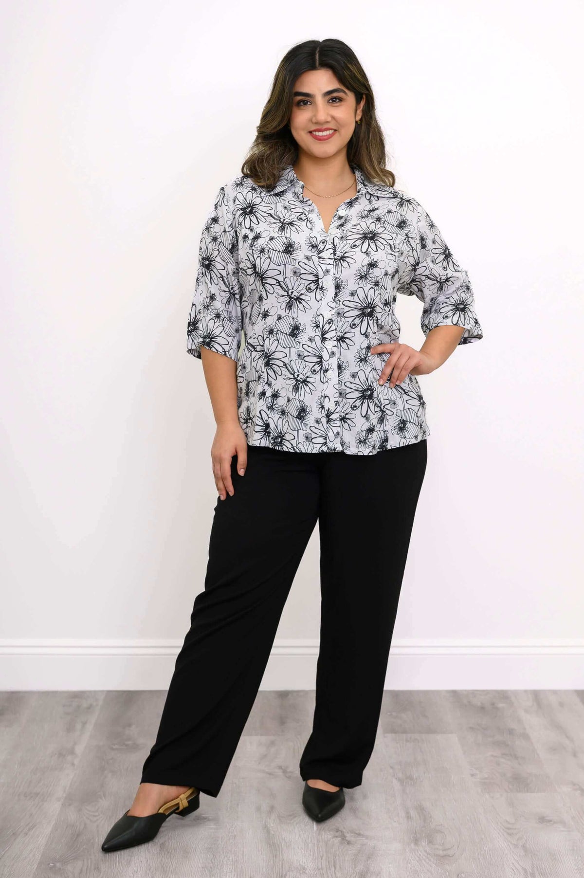 Woman posing in a white floral blouse and black pants