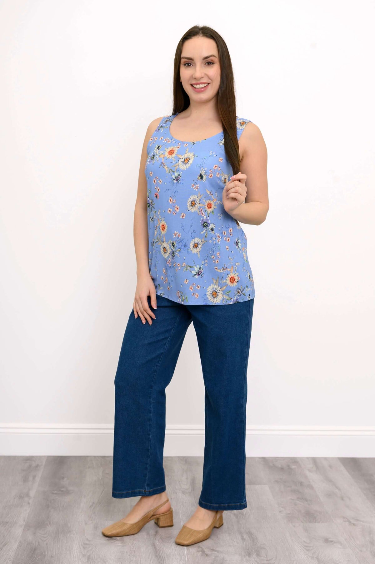 Woman wearing floral blue tank top and jeans, hand holding her hair