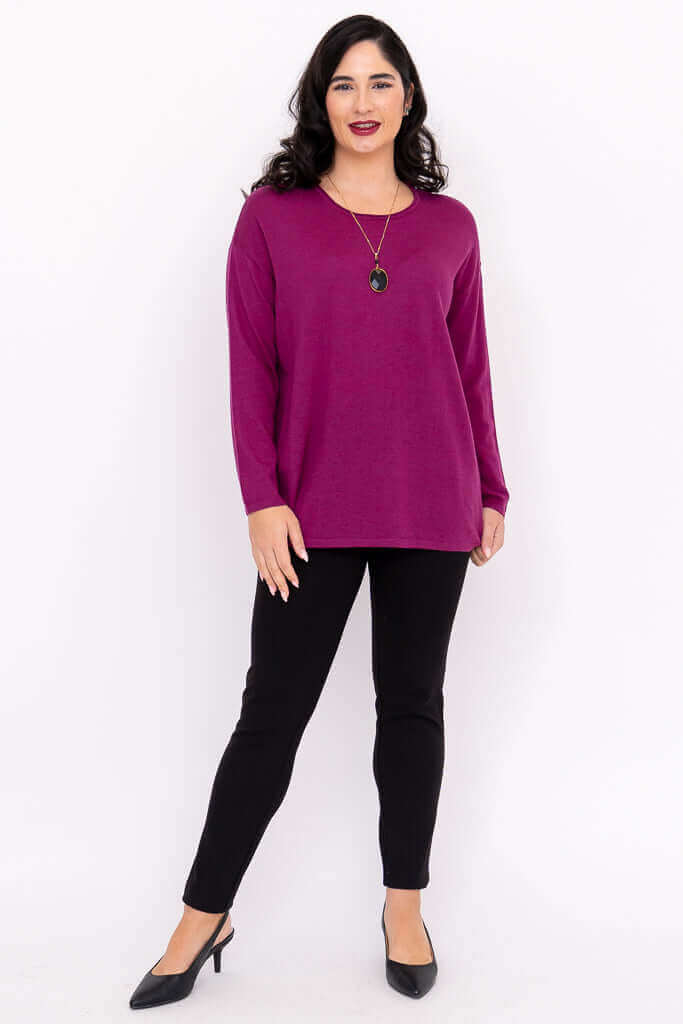 Woman posing in fuchsia sweater and black pants styled with necklace and heels