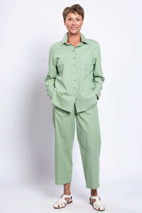 Woman smiling in full outfit with light green button-up shirt and matching trousers