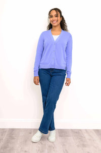 Woman posing in light purple cardigan, blue jeans, and white sneakers
