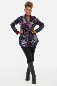 Woman with arms on hips wearing a long sleeve abstract print tunic and black pants