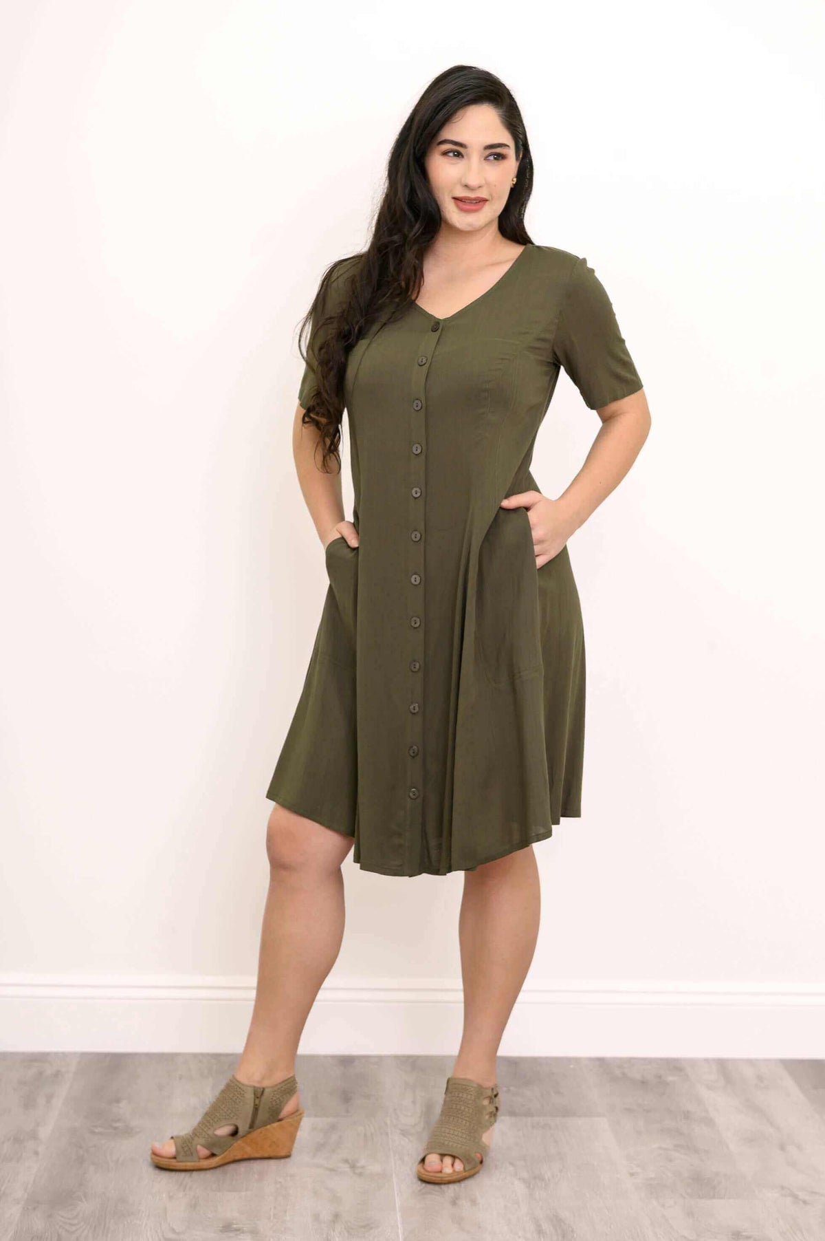 Woman posing in olive dress with hands in pockets, button-front detail visible