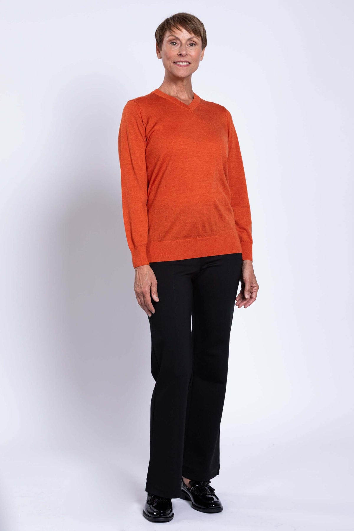 Woman posing in orange V-neck sweater and black dress pants