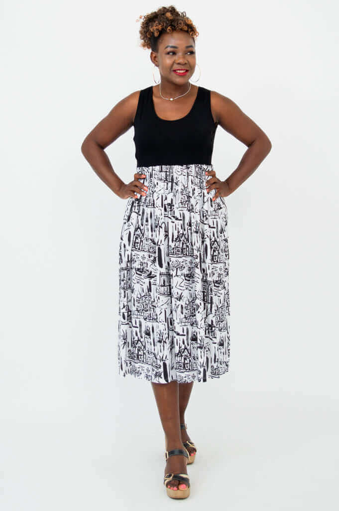 Woman standing in a sleeveless black and white city print midi dress with hands on hips