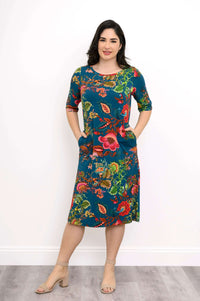 Woman in a teal floral bamboo dress with hands in pockets, front view