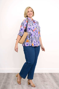 Woman posing with beige tote bag, wearing a purple floral button-up shirt and jeans