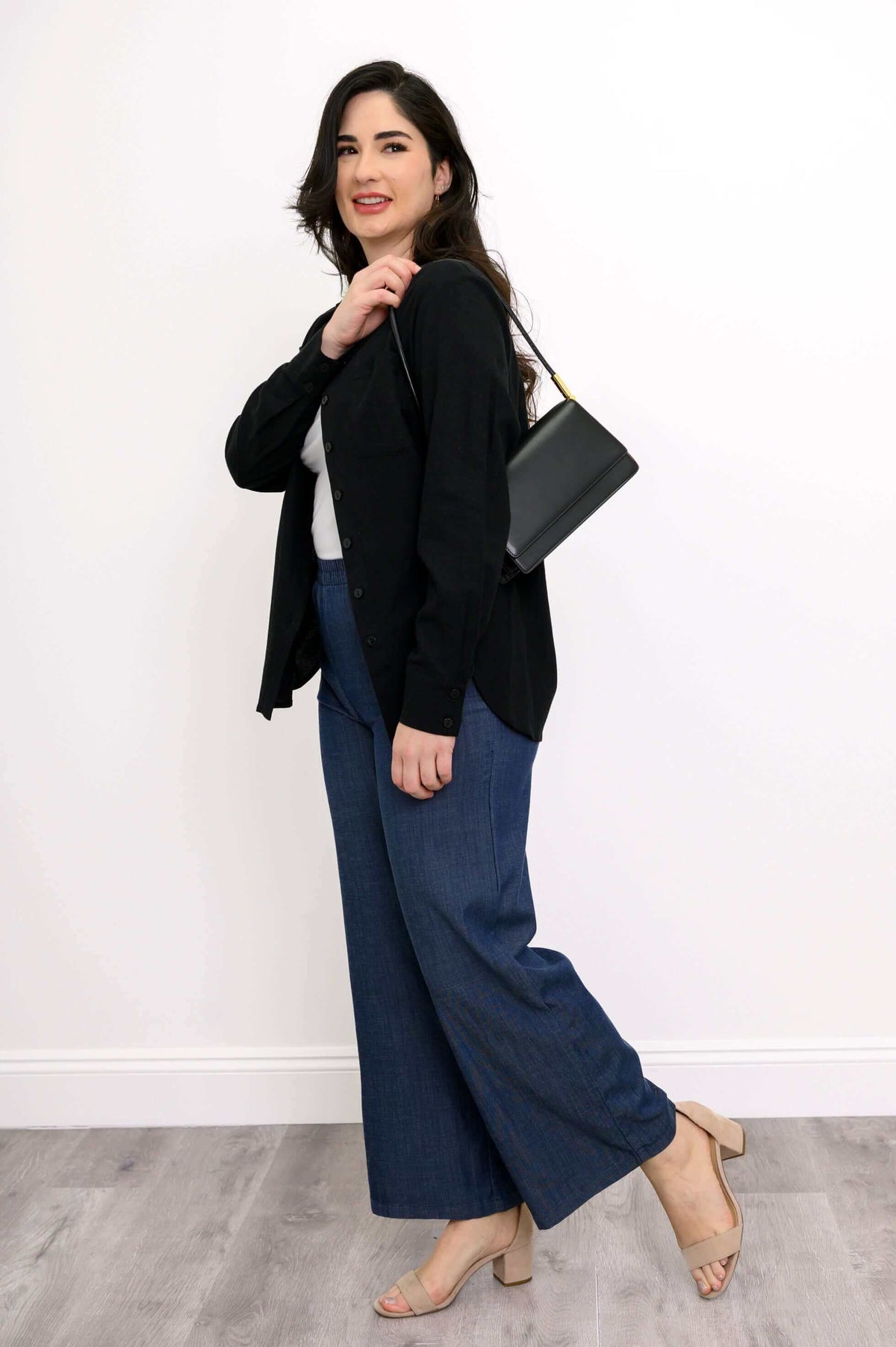 Woman in black button-up shirt and blue pants, posing with a black purse over her shoulder