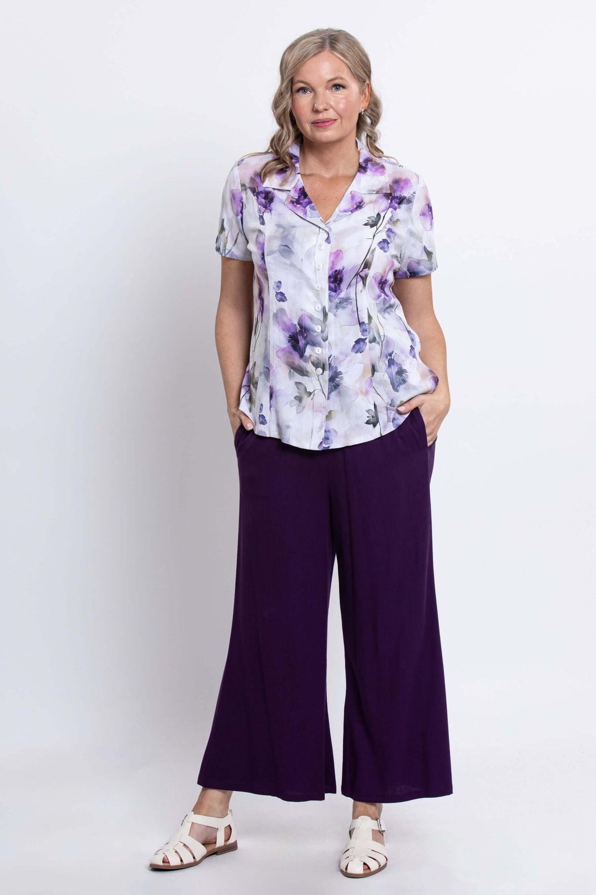 Woman standing with hands in pockets, wearing a floral shirt and purple pants, full body, front view