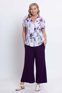 Woman standing with hands in pockets, wearing a floral shirt and purple pants, full body, front view