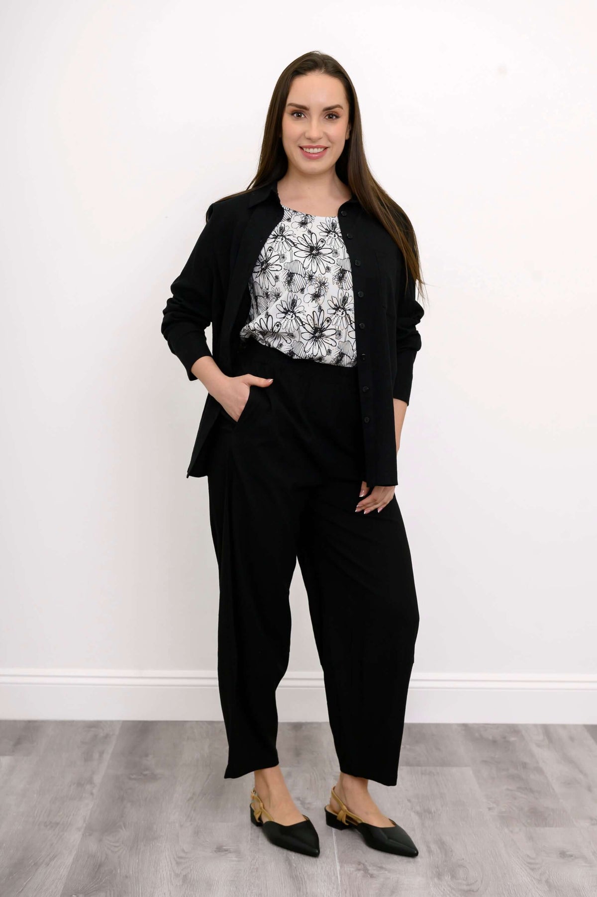 Woman showcasing black barrel-leg pants with floral blouse and black open cardigan