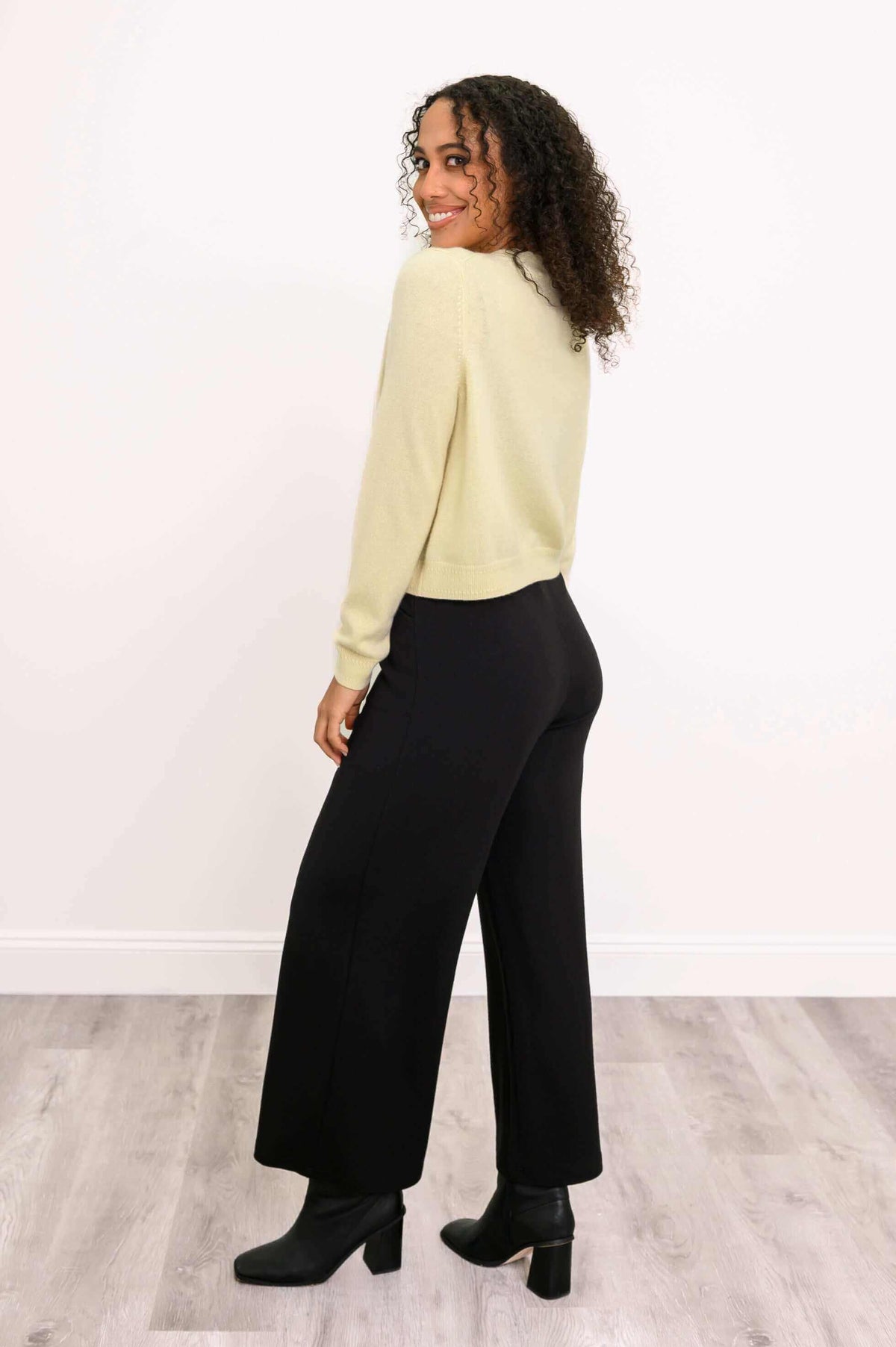 Woman showing back and side view of a light yellow cardigan, looking over shoulder