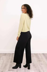 Woman showing back and side view of a light yellow cardigan, looking over shoulder