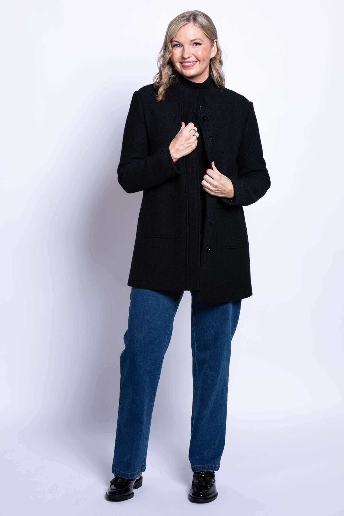 Woman smiling and holding open front of her black boiled wool coat, showing hidden snaps