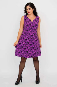 Woman showing pockets in a purple patterned shift dress