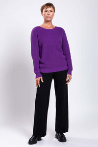 Woman showing the back of a purple shaker stitch sweater with center seam detail