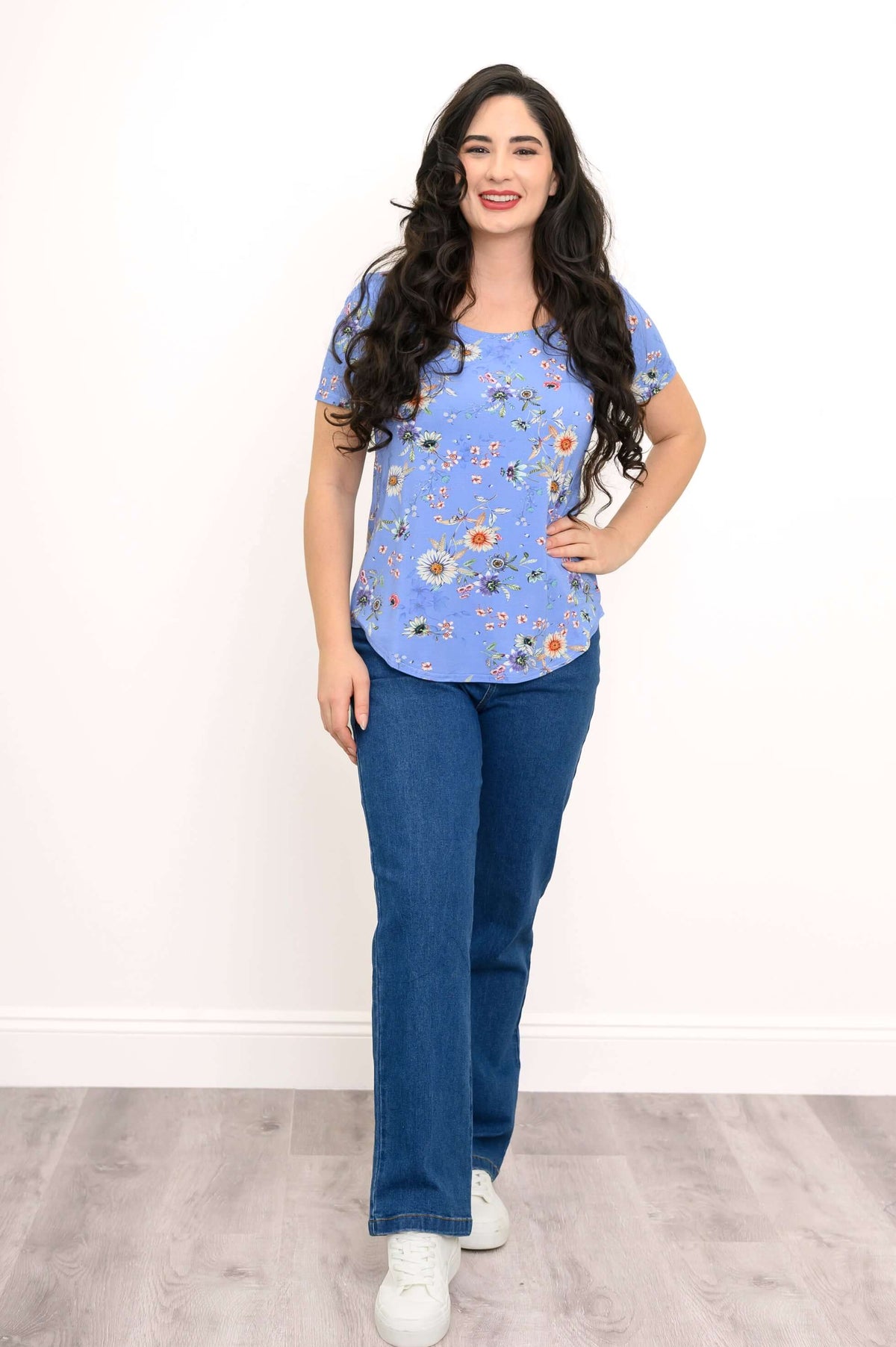 Woman smiling and standing in a blue floral bamboo tee and jeans, hand on hip
