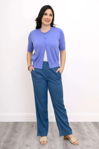 Woman smiling in a lavender cardigan, hands in pockets, front view