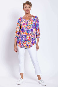 Woman smiling in a floral bamboo top paired with white pants and white shoes