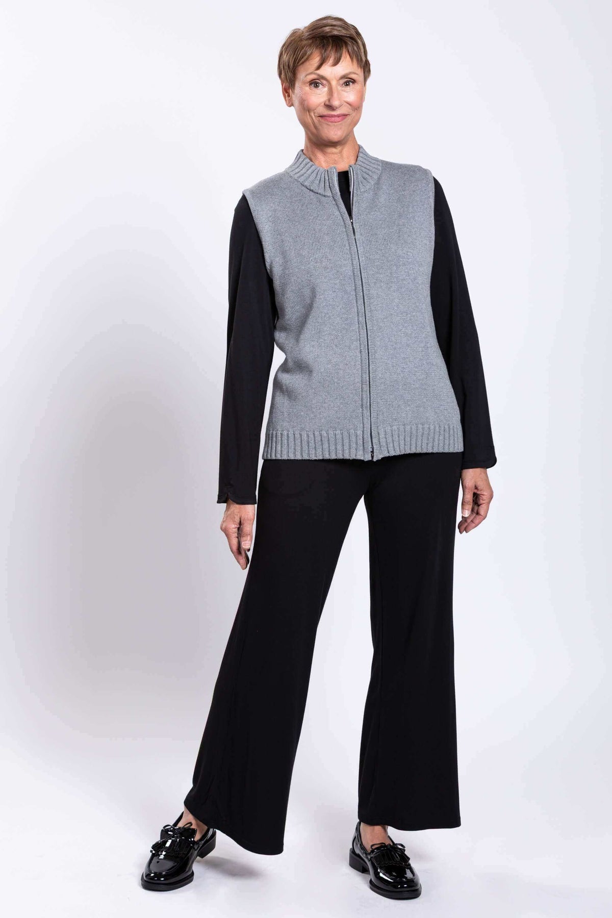 Woman smiling in a gray sleeveless zip vest, paired with black long sleeve top and pants