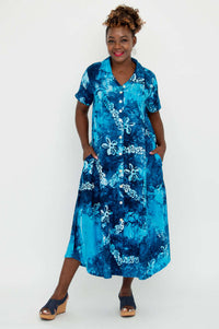 Woman smiling in a blue batik dress with hands in pockets, posing playfully