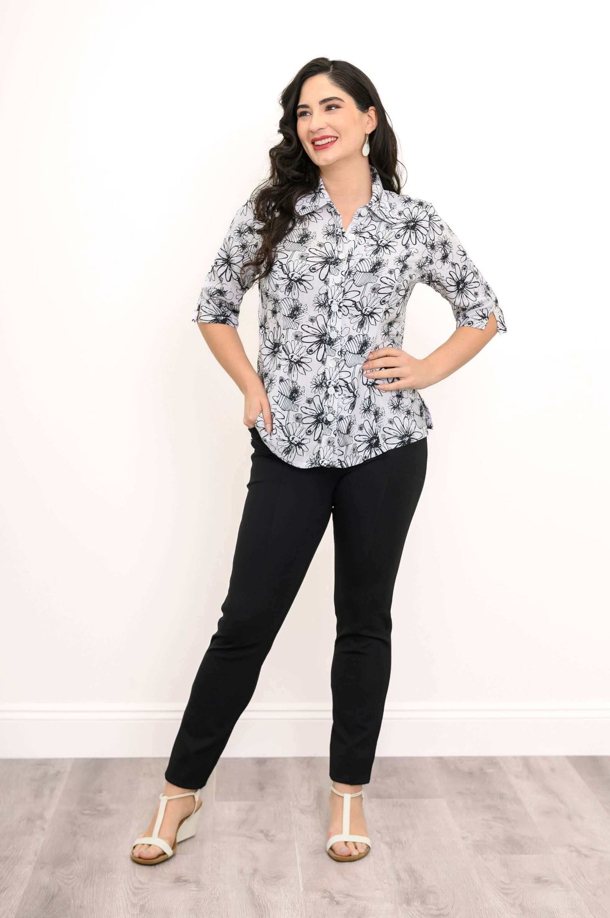 Woman smiling in a floral blouse and black pants with hands on hips