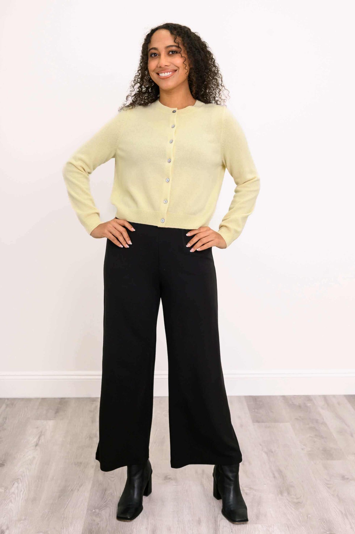 Woman smiling in a light yellow cashmere cardigan, hands on hips