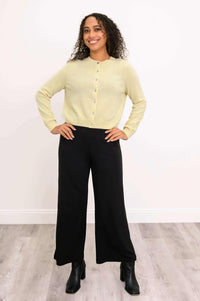 Woman smiling in a light yellow cashmere cardigan, hands on hips
