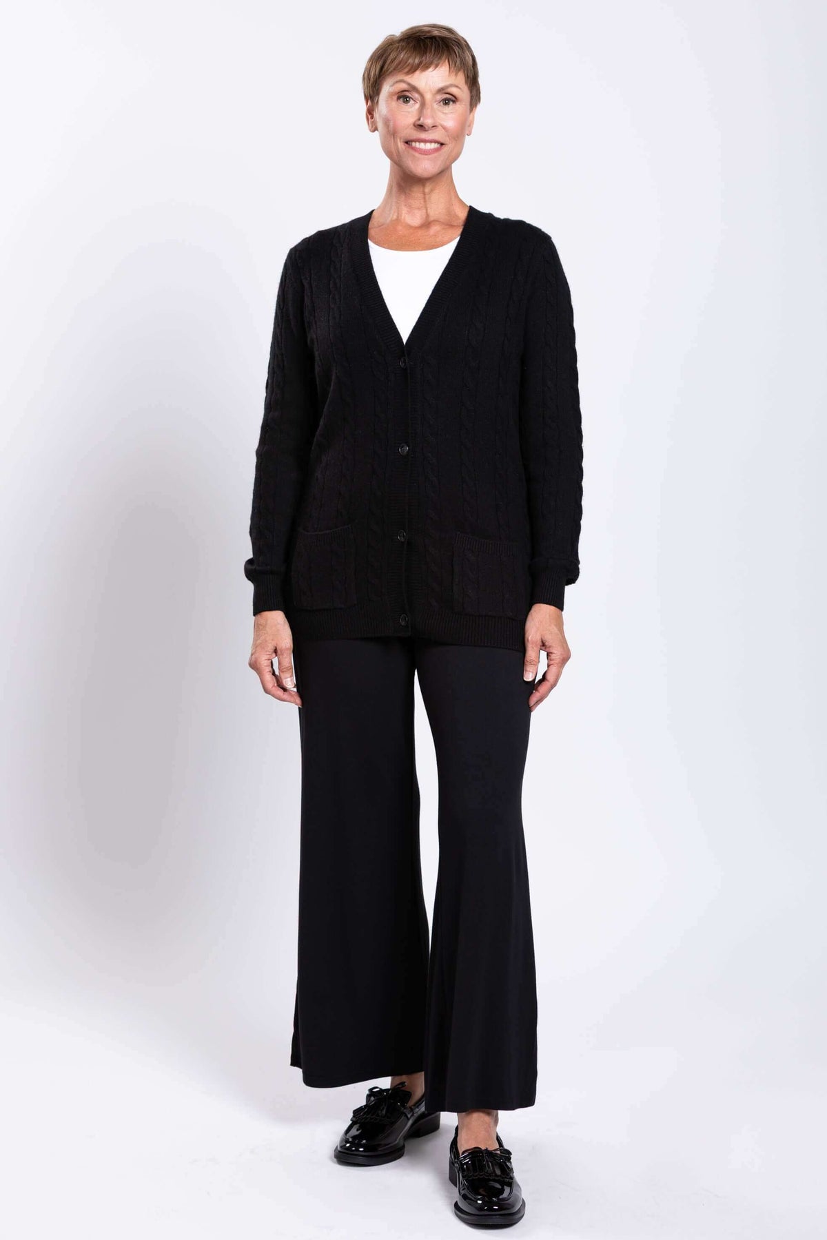Woman smiling in a black cable knit cardigan and black pants with tassel loafers