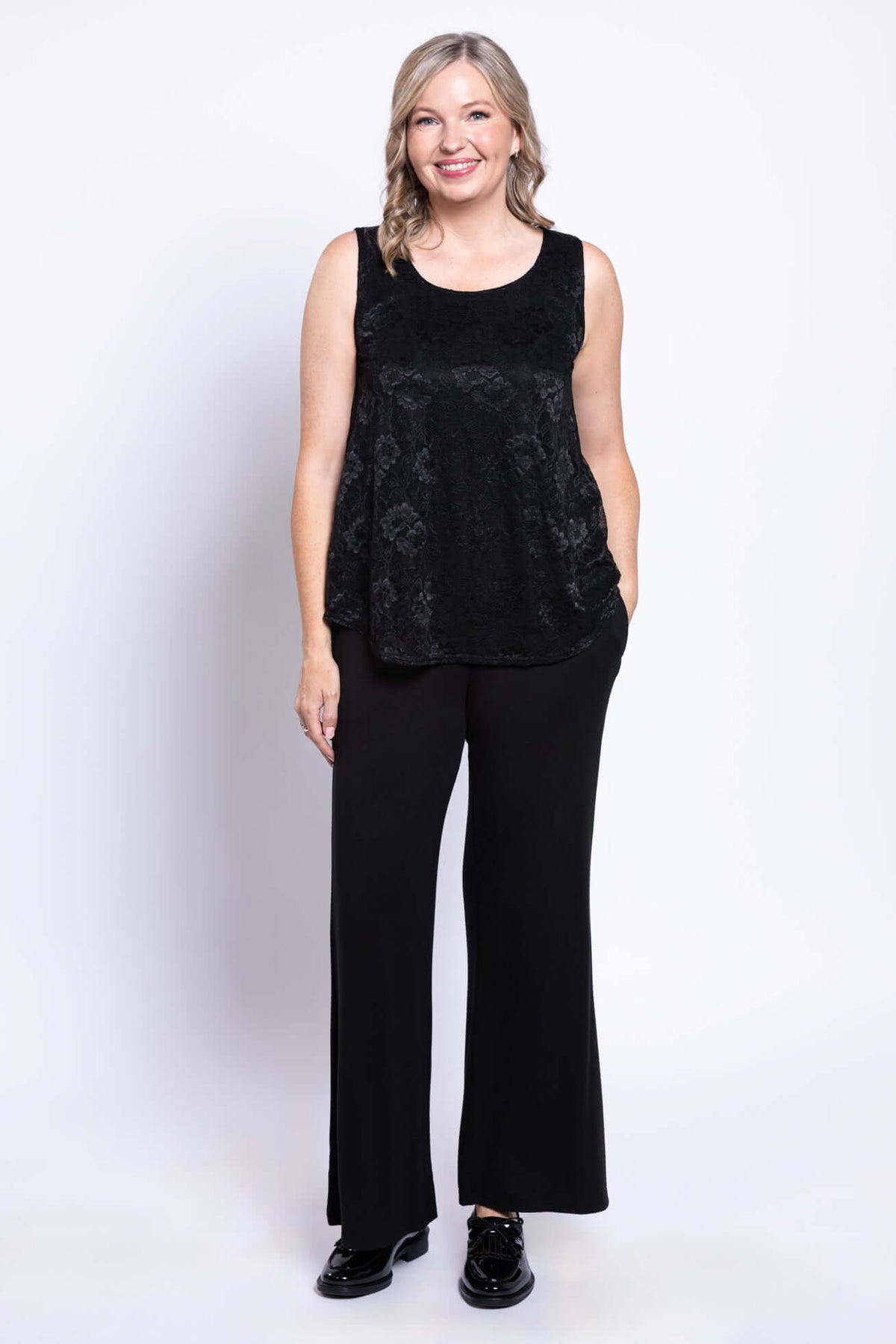 Smiling woman stands in a black lace tank top and black wide-leg pants