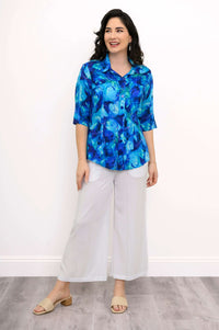 Woman smiling in blue watercolor print blouse and white wide-leg pants