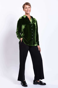 Woman posing with hand in pocket, green silk velvet blouse and black pants, smiling