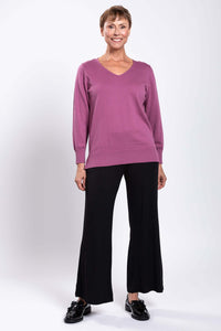 Woman smiling in mauve V-neck sweater and black pants, facing forward