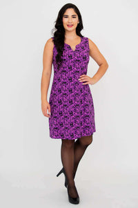 Woman smiling in a purple patterned shift dress, hand on hip