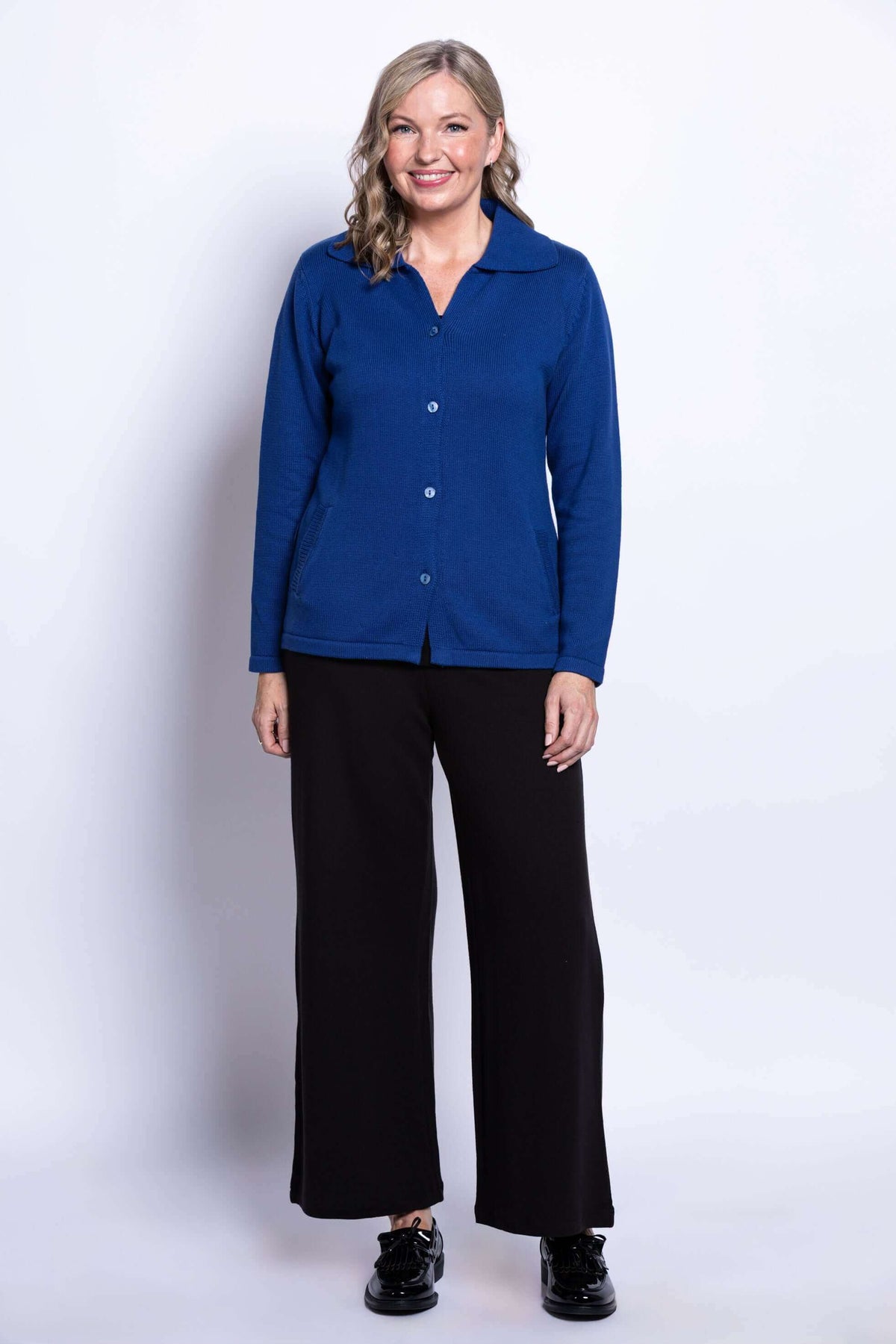 Woman smiling in fully buttoned royal blue Lily Cardigan and wide black pants