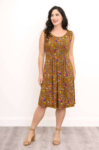 Woman smiling in a brown sleeveless floral dress, relaxed pose with pleated detailing