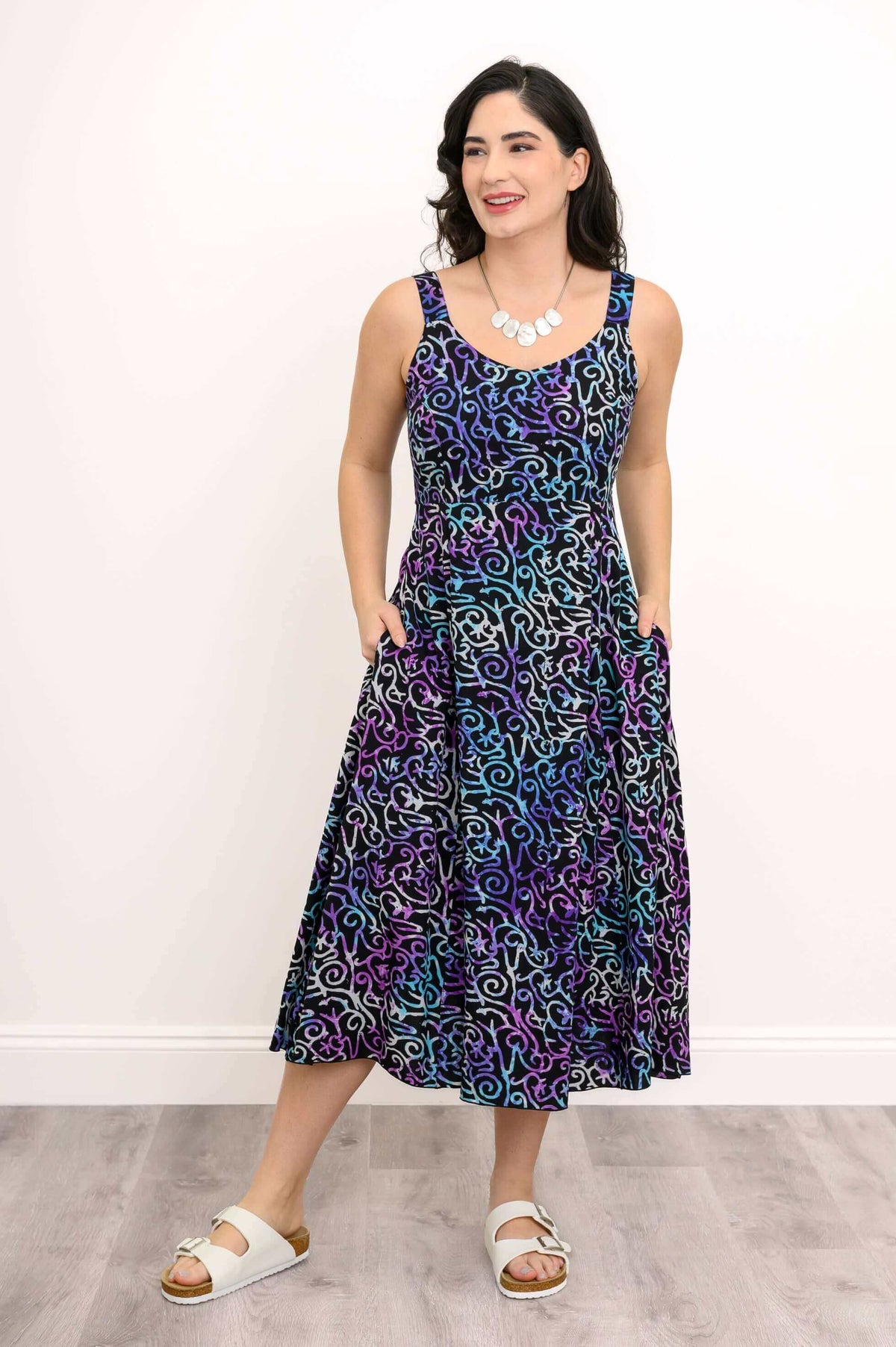Smiling woman wearing a sleeveless empire waist dress with pockets, multicolor swirl pattern