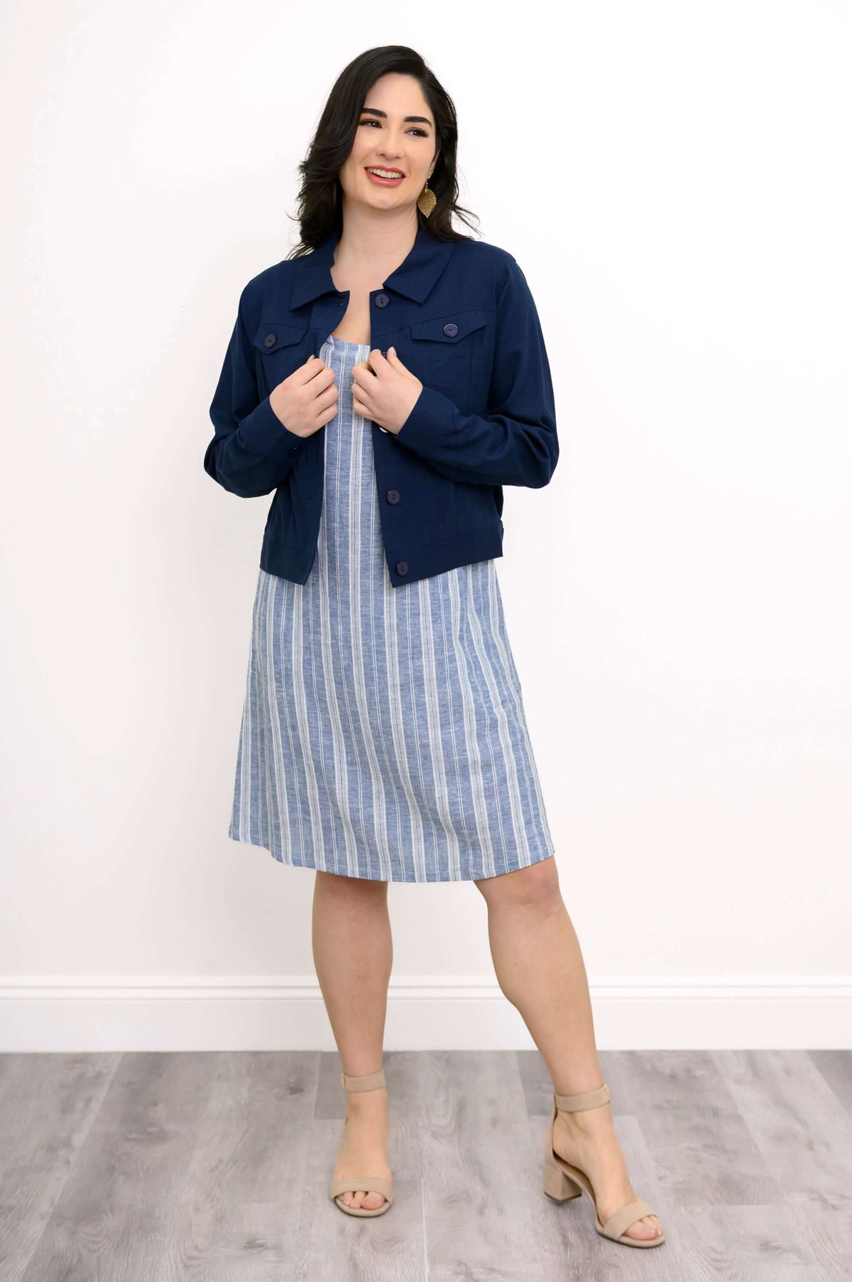 Woman smiling in blue and white striped dress with navy jacket, hands on jacket