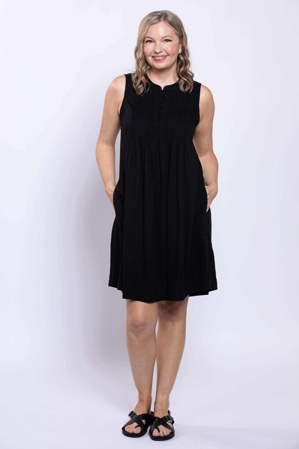 Woman smiling with hands in pockets in black pintuck A-line dress